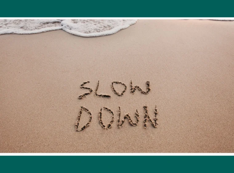 Spokojna plaża i napisane na pisaku palcem albo patykiem: Slow down. Zdjęcie wprowadzające do artykułu Uważność: jak zacząć być „tu i teraz”